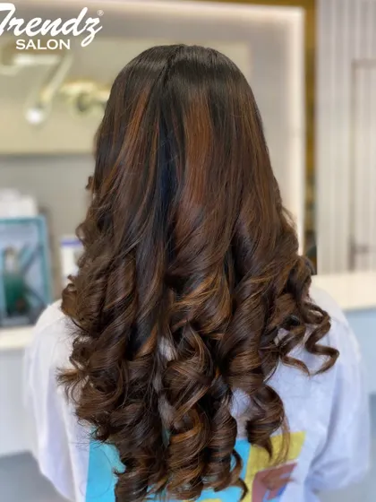 A close-up of a beautiful hair color and styling. The rich brunette tones are enhanced by bouncy curls, showing off the hair's health and shine.