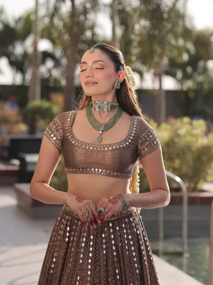 A serene moment captured. The bride's bronze lehenga and green jewelry create a beautiful contrast, showcasing a look that is both traditional and refreshingly modern.