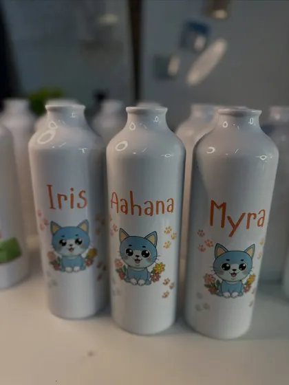 A set of three personalized bottles with the same cute cat design, customized with different names for a birthday party order.