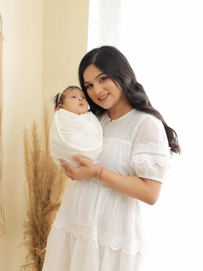 A beautiful mother smiling at the camera while holding her swaddled newborn. This is a classic portrait that captures the joy and pride of new motherhood.