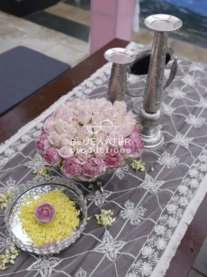 A traditional table setting with a lace runner, silver candle holders, and a delicate arrangement of pink roses.