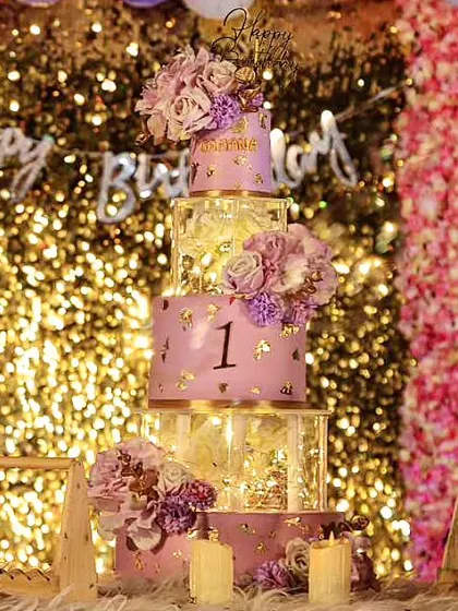 A magnificent five-tier lavender cake for a first birthday celebration. The combination of lighted spacer tiers and a glittering backdrop made this a true showstopper.