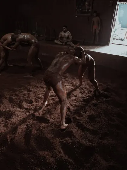 Action shots from inside the taleem, showing wrestlers locked in combat. The low lighting and shadows emphasize the raw power and technique of the grappling matches.