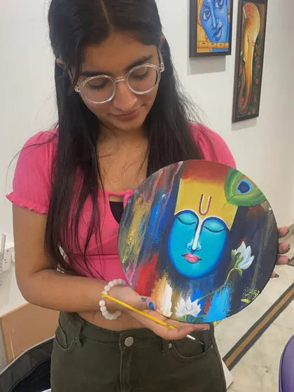 A student proudly holds her finished abstract Krishna painting on a round canvas. This piece beautifully blends vibrant colors and textures to create a modern interpretation of a classic spiritual subject.