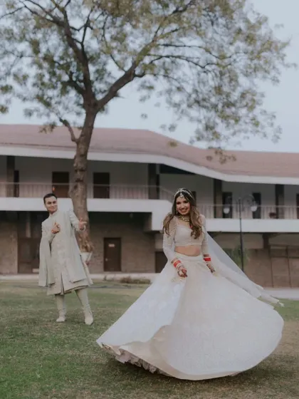 The bride twirls in her beautiful white lehenga while the groom looks on with a smile. A playful and happy moment.