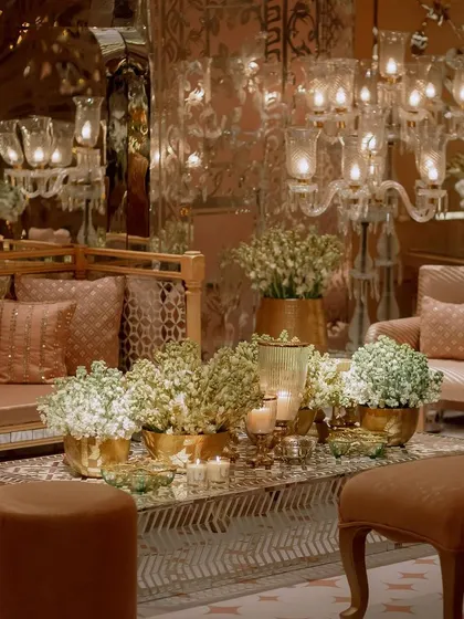 A detail shot of a lounge area with a mirrored backdrop. The space is filled with dozens of candles and fresh white flowers, creating a warm, shimmering, and inviting corner for guests.