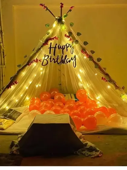 A cozy teepee tent setup for a birthday. The tent is decorated with fairy lights and filled with orange balloons, creating a perfect spot for a private celebration.