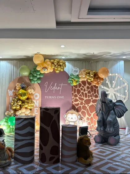 A sophisticated jungle-themed first birthday stage. This setup features large animal props like a giraffe and elephant, animal-print pedestals, and a custom backdrop with the child's name.
