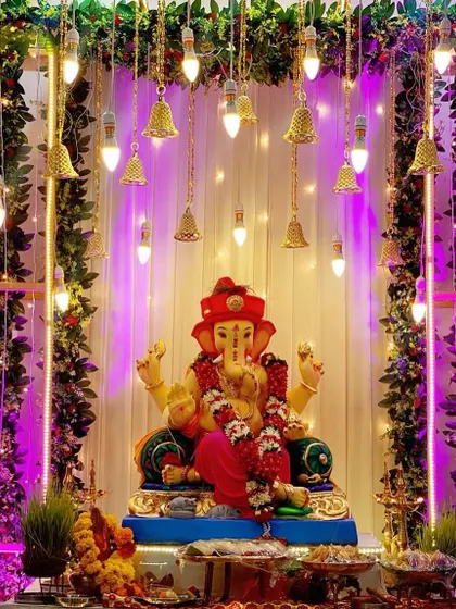 A beautiful Ganpati mandap featuring a canopy of green vines and hanging lighted bells. The purple lighting creates a magical and devotional atmosphere.