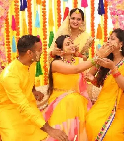 A candid moment of fun during a Haldi ceremony. The decor, with its bright yellow and pink floral backdrop, enhances the joyful and celebratory mood of the event.