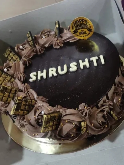 This rich chocolate cake for Shrushti is all about indulgence. It features a glossy chocolate ganache top, piped chocolate buttercream, and mini chocolate bars dusted with edible gold.