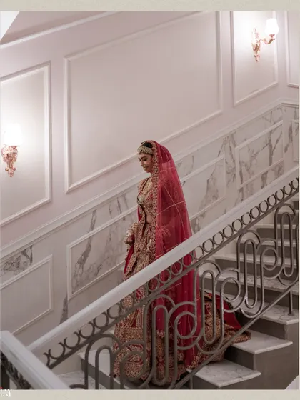 The bride descends a grand marble staircase, looking like royalty in her red wedding lehenga.