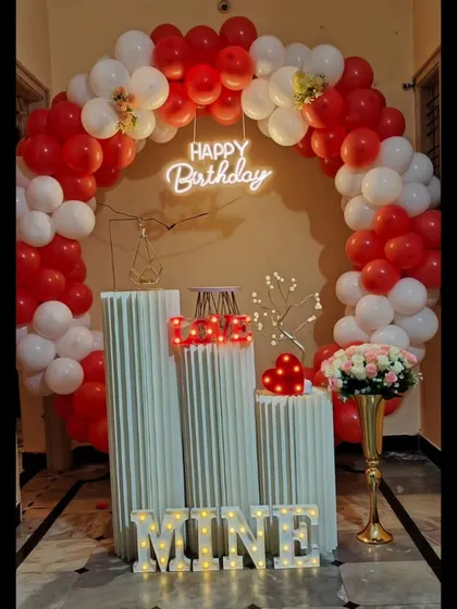 A classic romantic birthday setup in red and white. The circular balloon arch, light-up letters spelling 'Mine' or 'My World', and soft lighting make for a very personal and heartfelt surprise.