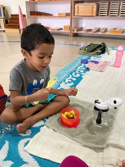 Snack time is a moment for independence and practicing grace and courtesy. This child is enjoying a healthy snack he served himself, sitting calmly in his chosen workspace.