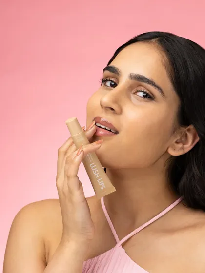 A close up lifestyle shot focusing on the application of a nude lip gloss. The model's relaxed expression and the soft lighting create a natural, effortless beauty look that is highly aspirable.