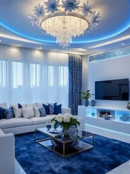 A living room designed with a vibrant blue color scheme. We used a blue area rug and matching cushions to create a cohesive look, complemented by blue ambient lighting in the ceiling cove and TV unit. The floral crystal chandelier adds a touch of whimsical elegance.