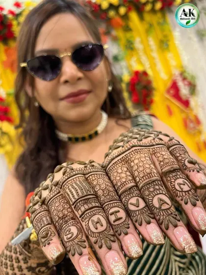 A happy client proudly displaying her personalized mehndi with the name 'SHIVAM' written across her fingers.