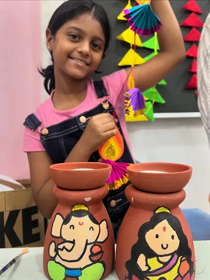 This student is thrilled with her finished Diwali crafts, including painted diyas and a paper hanging.