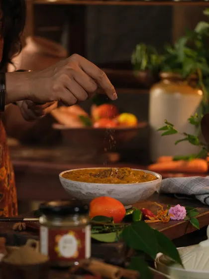 An action shot of a hand sprinkling spices over a dish, demonstrating the product in use and adding a dynamic element to the photograph.