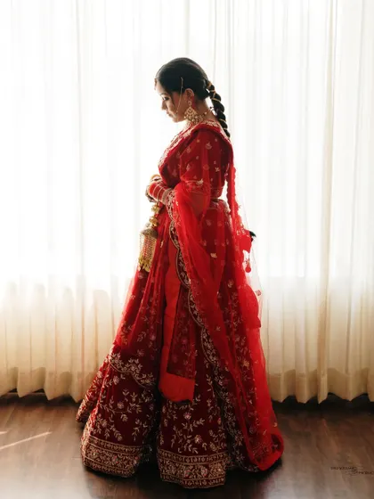 A silhouette of the bride against a brightly lit window. This artistic shot creates a sense of mystery and highlights the beautiful form of her red wedding lehenga.