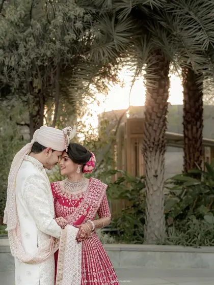 An intimate portrait against a backdrop of palm trees at sunset. The warm light and close embrace make this a deeply romantic and timeless wedding photograph.