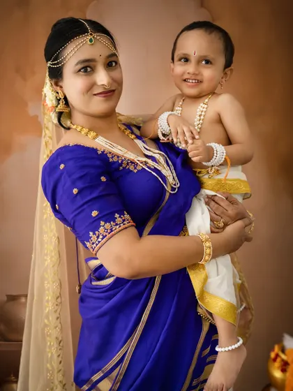 A smiling portrait of a mother and her happy baby boy, both dressed in their festive best for Janmashtami.