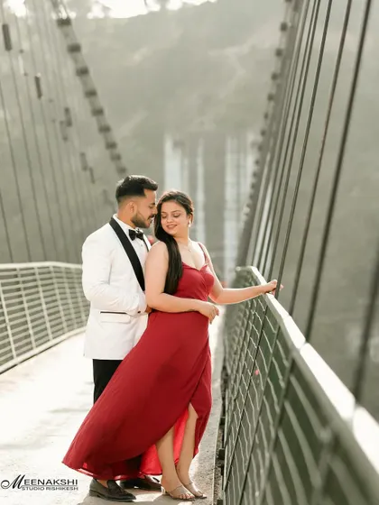 A romantic shot of a couple on a bridge, with the groom in a white tuxedo and the bride in a flowing red dress. The leading lines of the bridge draw the eye directly to them.