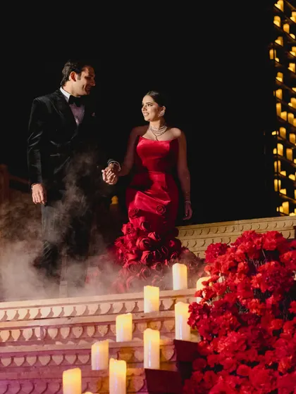 The couple makes a grand entrance down steps lined with red roses and candles, with smoke effects adding to the drama and romance of the moment.