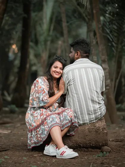 A relaxed and candid pre-wedding photo of a couple sitting together in a grove of trees, capturing a moment of quiet intimacy and happiness.