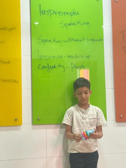 This student is about to begin his impromptu speech based on a small toy. The goal is to build fluency and confidence, turning nervousness into creative energy.