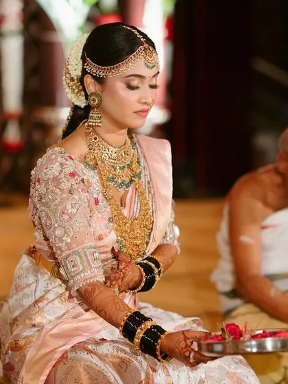 A close-up of the bride during her wedding ceremony. The delicate embroidery on her pastel blouse and her traditional jewelry create a look of timeless elegance.
