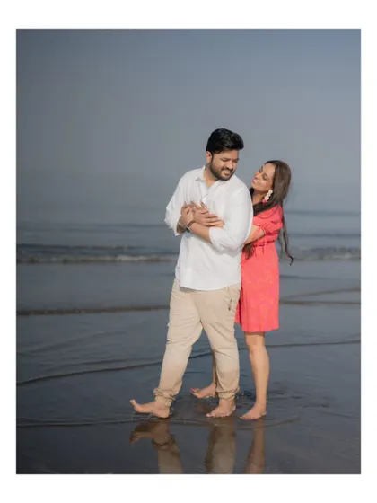 A playful and romantic moment on the beach, with the bride hugging the groom from behind as they stand by the sea.