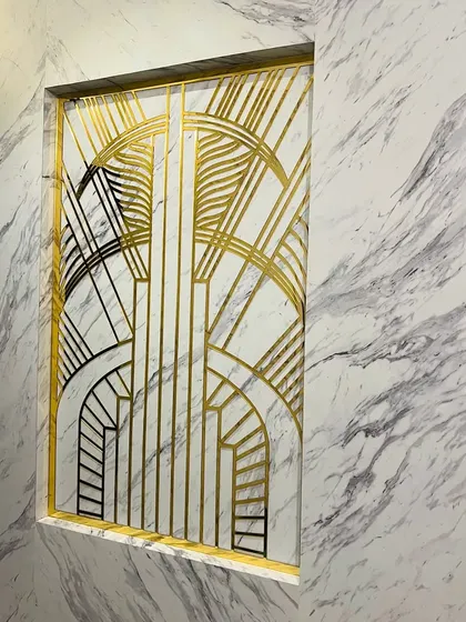 To make a memorable first impression, we created this Art Deco-inspired partition for an entryway. The custom-designed geometric pattern in gold and black metal set against a marble-finish wall adds a touch of timeless glamour.