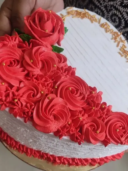 This cake showcases intricate piping work with a cascade of red buttercream roses. A sprinkle of golden jimmies adds a final touch of elegance to the clean white design.