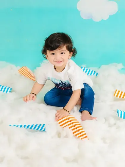 A toddler plays with paper airplanes in a sky-themed setup, his imagination taking flight.