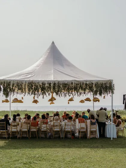 A beautiful beachside wedding lunch under a large white tent, with hanging floral decor that adds a touch of elegance to the natural setting.