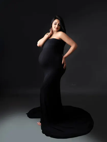 This pose beautifully showcases the baby bump. The mom-to-be looks stunning in a simple, strapless black bodycon gown against a moody, dark backdrop.