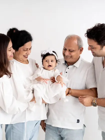 A timeless multigenerational family portrait, celebrating the connection between grandparents, parents, and their new baby. The coordinated white outfits and clean background create a classic, elegant look that will be cherished for years.
