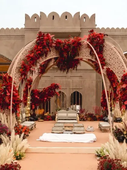 A closer look at the open-air mandap, where intricately designed arches are adorned with bold red florals and soft pampas grass. This design blends traditional color palettes with contemporary textures for a regal feel.