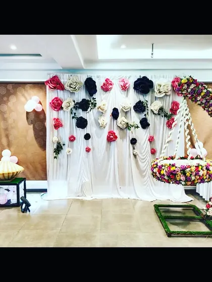 A naming ceremony decoration with a hanging floral cradle and a backdrop of large paper flowers in multiple colors, creating a vibrant and festive look.
