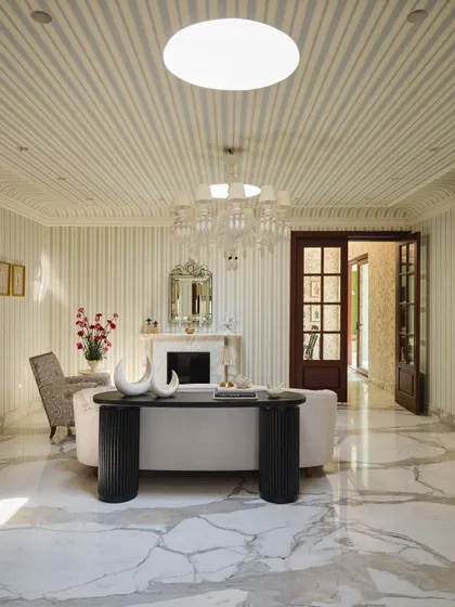 The salon, or formal living room, is a stage set for conversations. Sunlight from twin skylights casts drama across striped walls, a restored fireplace, and a mix of sculptural and classic furniture.