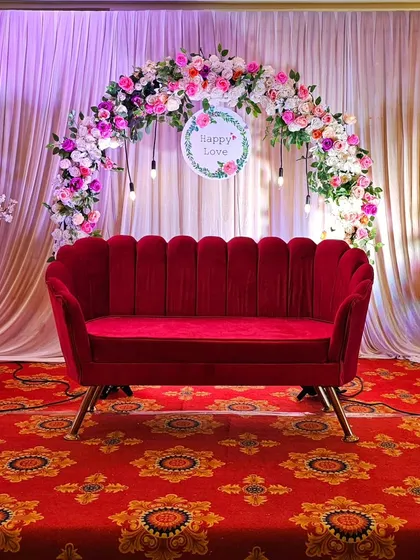A full view of the elegant stage with the red velvet sofa and floral arch.