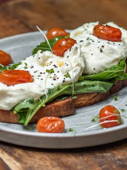 Our creamy, house-made burrata served over arugula and blistered cherry tomatoes on a thick slice of our toasted sourdough bread. A truly happy morning starts here.