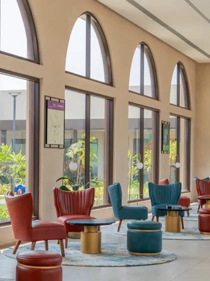 The lounge area is furnished with colorful, plush chairs in shades of red and blue, set against a backdrop of tall arched windows.