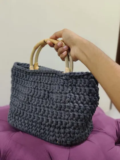 A hand holding the sturdy bamboo handle of the grey T-shirt yarn basket bag, showing its practical design.