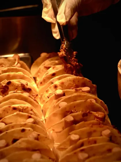A chef carefully adding fillings to a line of tacos at the live bar. This setup allows for efficient service while maintaining a high level of quality and presentation.