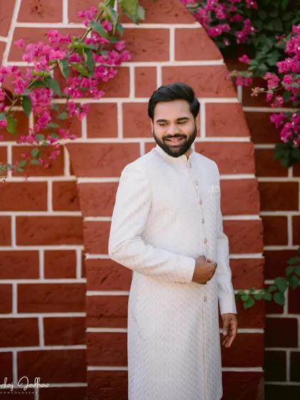 A smiling portrait of the groom, Shantanu, looking elegant in his white sherwani.