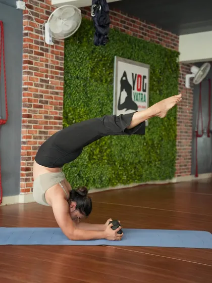 Vrschikasana (Scorpion Pose) in Pincha Mayurasana, using a dumbbell for added wrist and forearm strengthening. This advanced variation combines a deep backbend with an inversion.