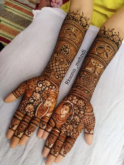 A full bridal design for a South Indian wedding, this piece features portraits of the couple surrounded by auspicious elements. The arms are decorated with panels showing Ganesha, a wedding invitation, and other traditional motifs.