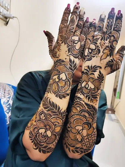 A beautiful pose showcasing the full extent of this intricate arm-length mehndi. The design features heart shapes and floral patterns, perfect for a bride.